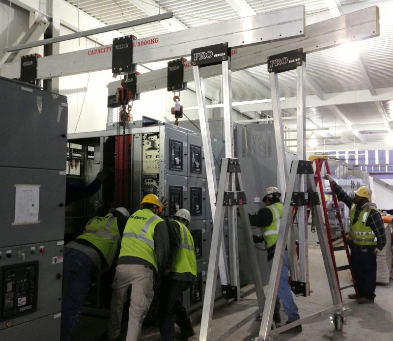 Three eme 11000 PRO Series aluminum gantry cranes deployed in a power-distribution equipment room around switchgear cabinets, with workers in yellow safety vests carrying out the install.